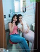 A couple of women sitting on top of a stool in a bathroom.