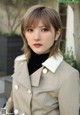 A woman wearing a beige trench coat and a black turtle neck sweater.
