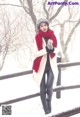 A woman in a white coat and red scarf standing in the snow.