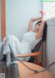 A woman in a white dress sitting in a chair.