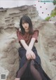 A woman sitting on top of a rock next to a rock wall.